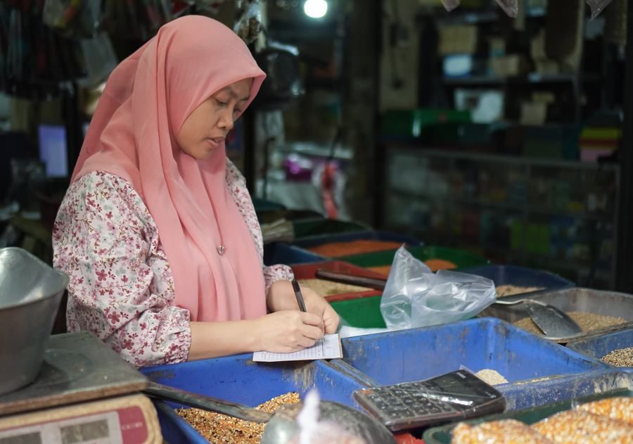 Pedagang perempuan berhijab mencatat penjualan di lapaknya
